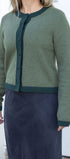 Person wearing a green cardigan over a navy skirt against a white background