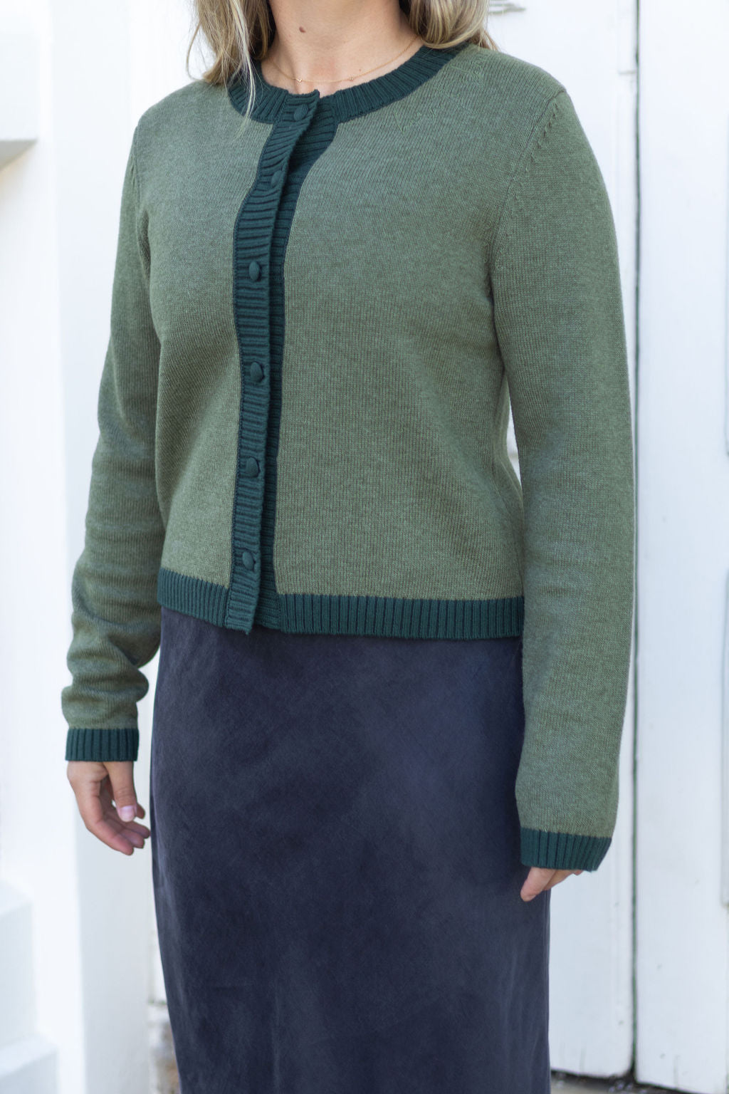 Person wearing a green cardigan over a navy skirt against a white background