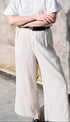 Person wearing a white shirt and light-colored pants against a textured wall.