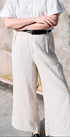 Person wearing a white shirt and light-colored pants against a textured wall.