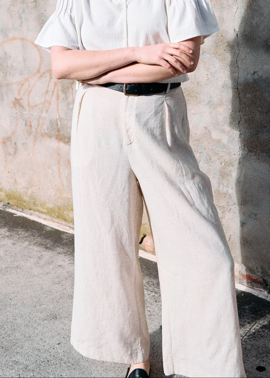 Person wearing a white shirt and light-colored pants against a textured wall.