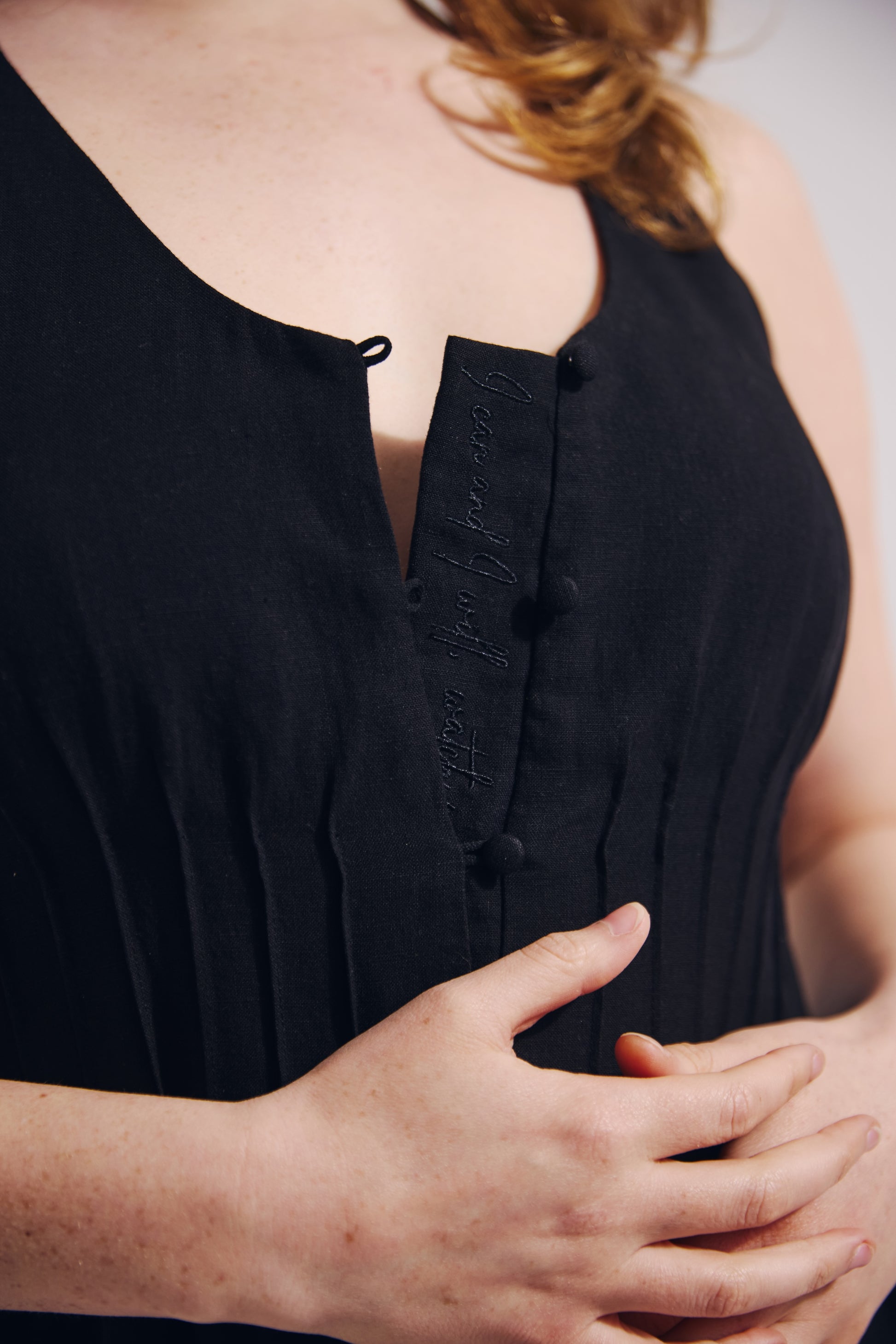 Close-up of a person wearing a black sleeveless top with button details.