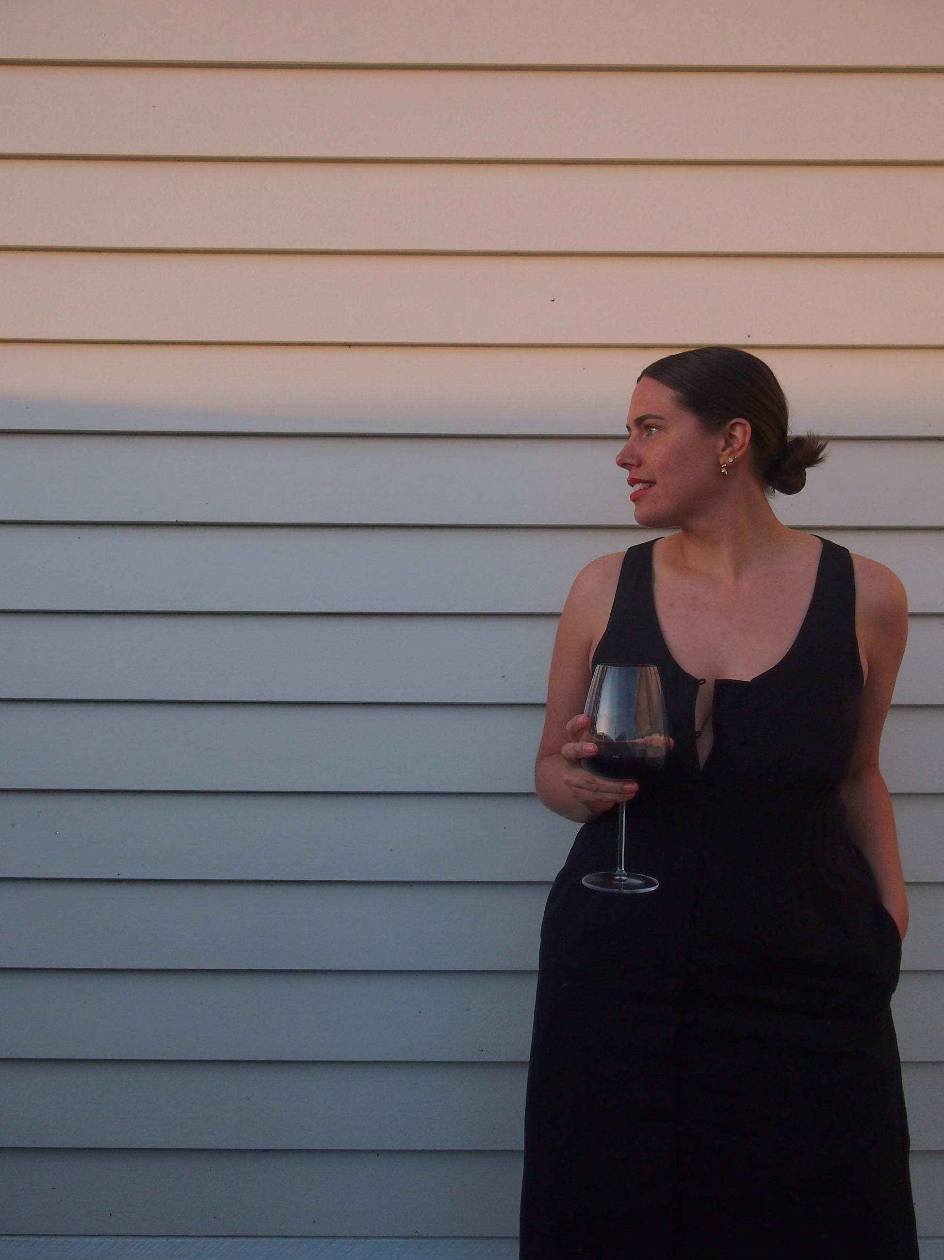Woman holding a glass of red wine against a light-colored wall.