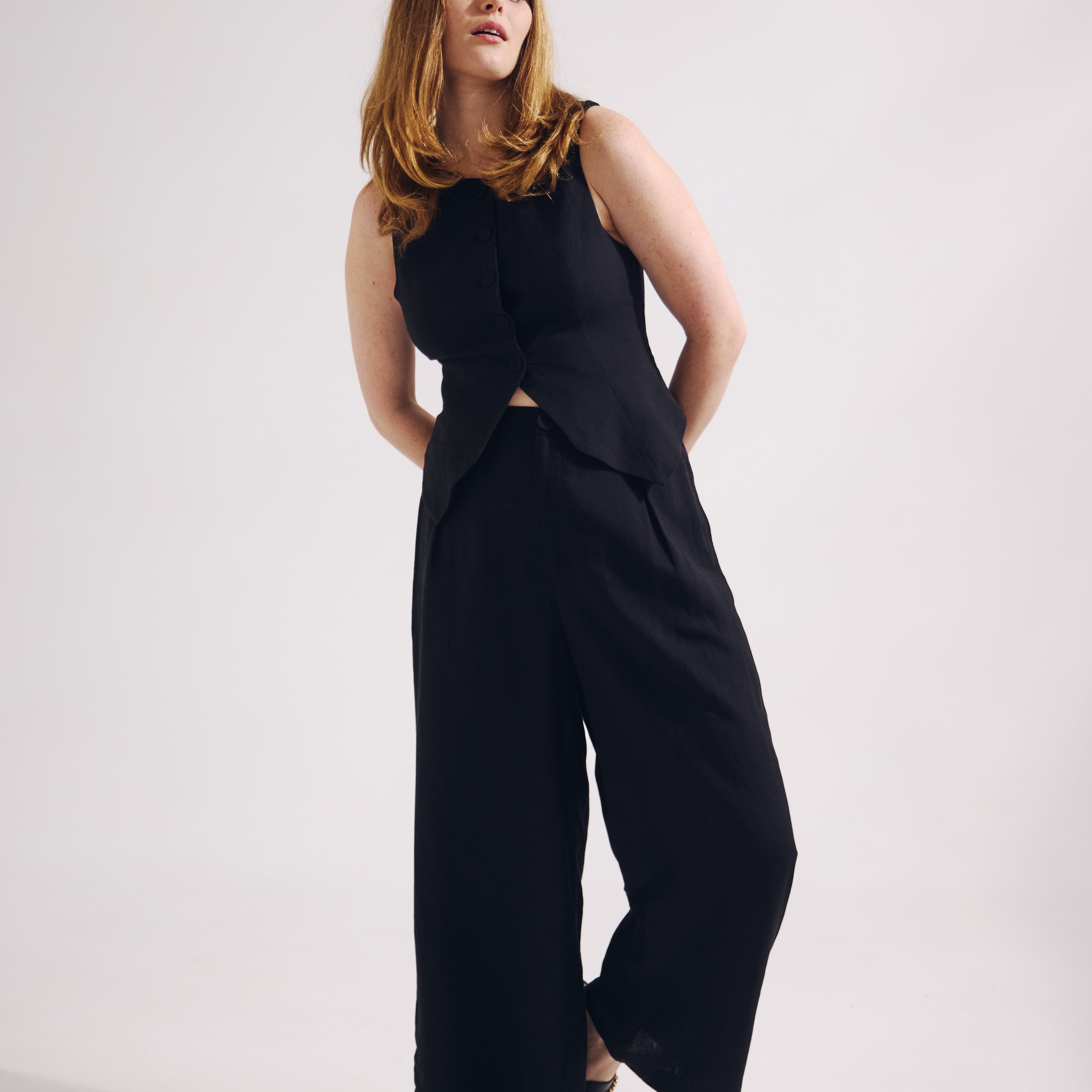 Woman wearing a black sleeveless top and wide-leg pants on a white background
