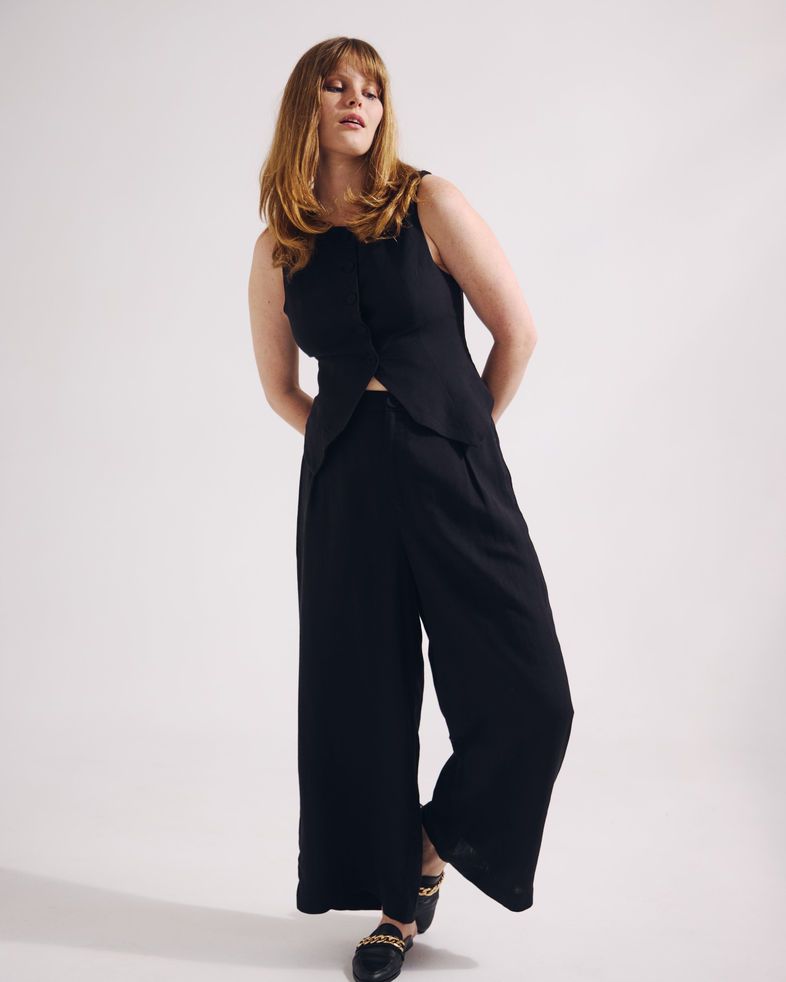 Woman wearing a black sleeveless top and wide-leg pants on a white background
