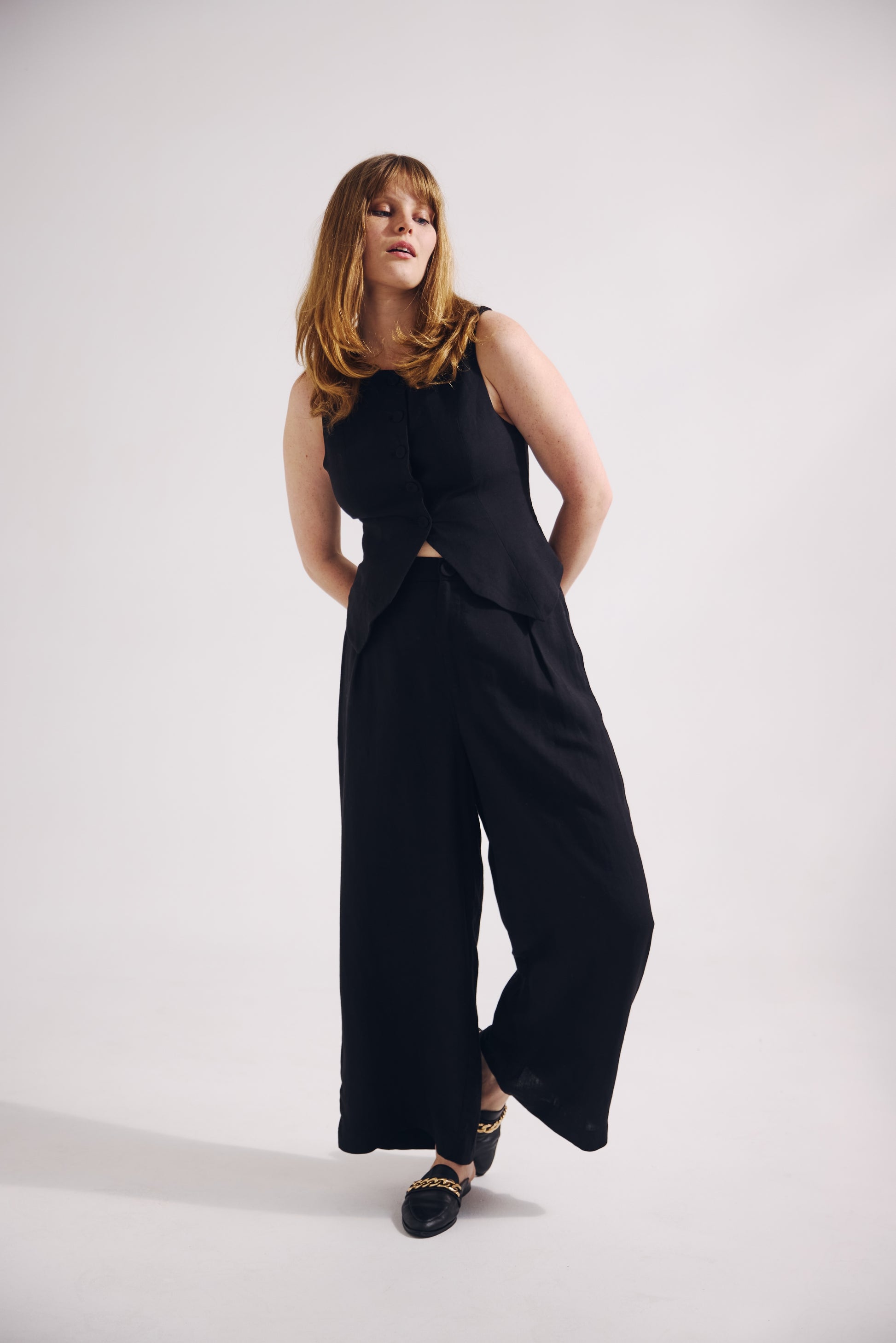 Woman wearing a black sleeveless top and wide-leg pants on a white background