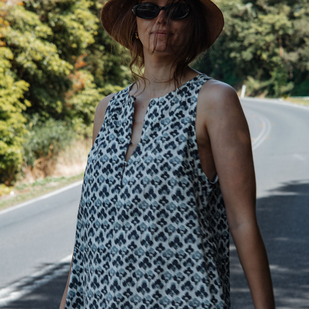 Woman wearing a patterned dress and hat on a road with trees in the background