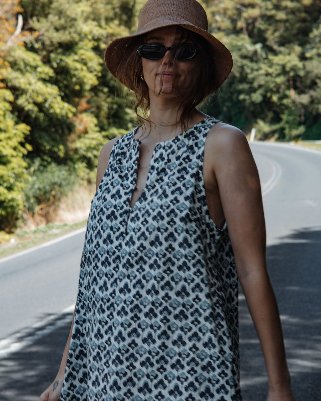 Woman wearing a patterned dress and hat on a road with trees in the background