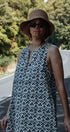 Woman wearing a patterned dress and hat on a road with trees in the background