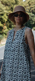 Woman wearing a patterned dress and hat on a road with trees in the background
