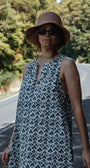 Woman wearing a patterned dress and hat on a road with trees in the background
