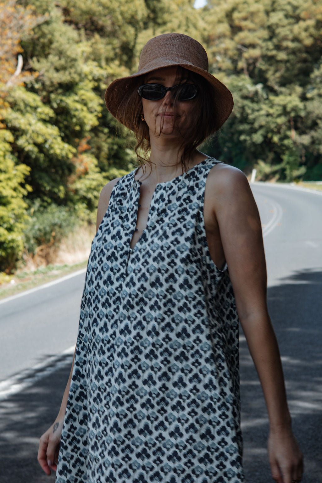 Woman wearing a patterned dress and hat on a road with trees in the background