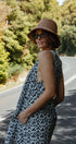 Woman in a leopard print dress and hat standing on a road with trees in the background