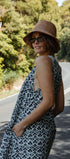 Woman in a leopard print dress and hat standing on a road with trees in the background
