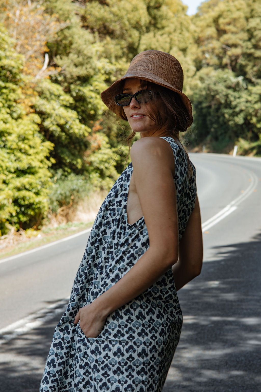 Woman in a leopard print dress and hat standing on a road with trees in the background