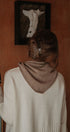 Person wearing a beige sweater with a brown hood in a room with a painting on the wall.