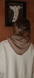 Person wearing a beige sweater with a brown hood in a room with a painting on the wall.