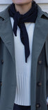 Person wearing a gray trench coat over a white sweater with a black scarf.
