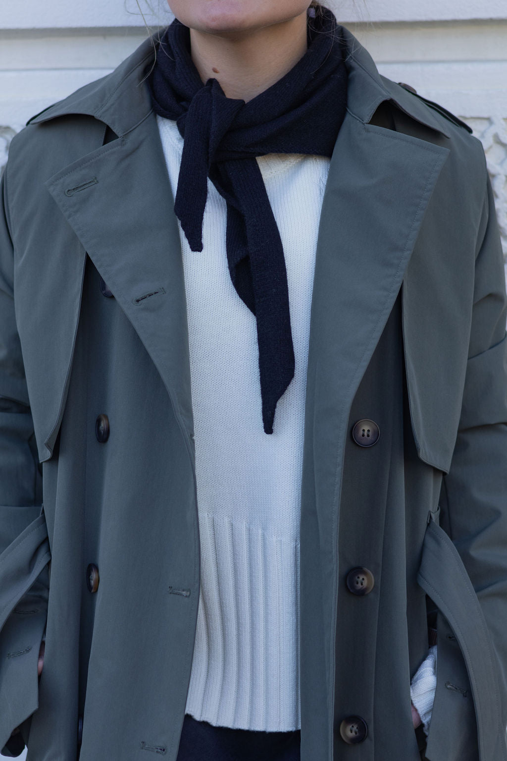 Person wearing a gray trench coat over a white sweater with a black scarf.