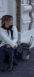 Woman sitting on steps wearing a white sweater and dark blue pants, with a basket nearby.