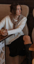 Woman sitting at a cafe table holding a cup, wearing a white sweater and black skirt.