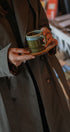 Person holding a green mug with a brown coat in an indoor setting