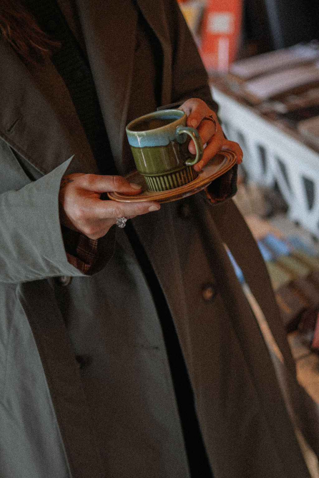 Person holding a green mug with a brown coat in an indoor setting