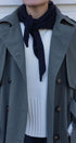 Person wearing a gray trench coat over a white sweater with a black scarf.