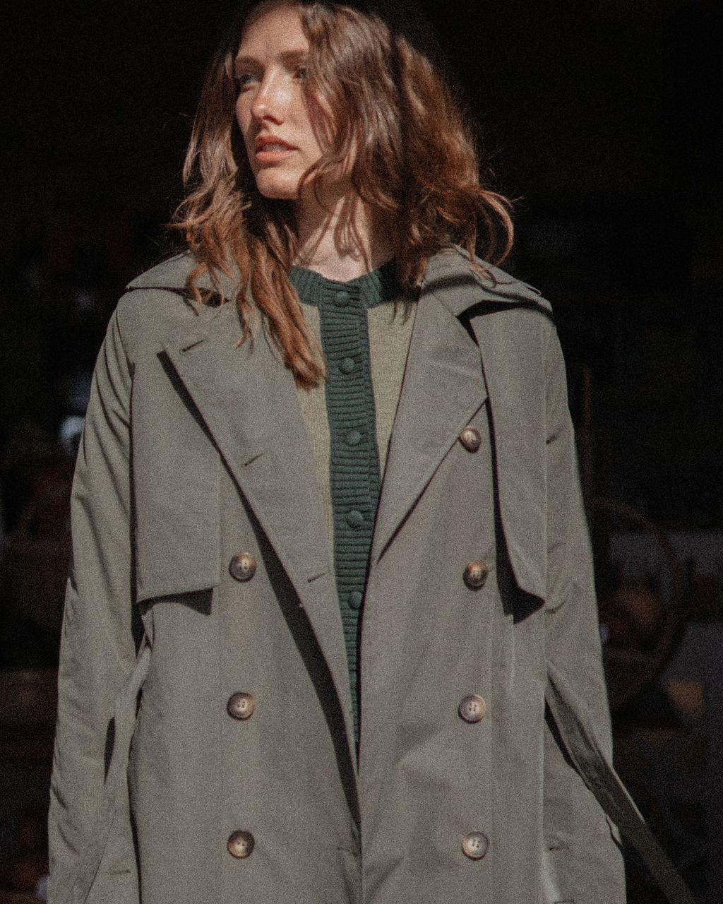 Woman wearing a long green coat with a dark background