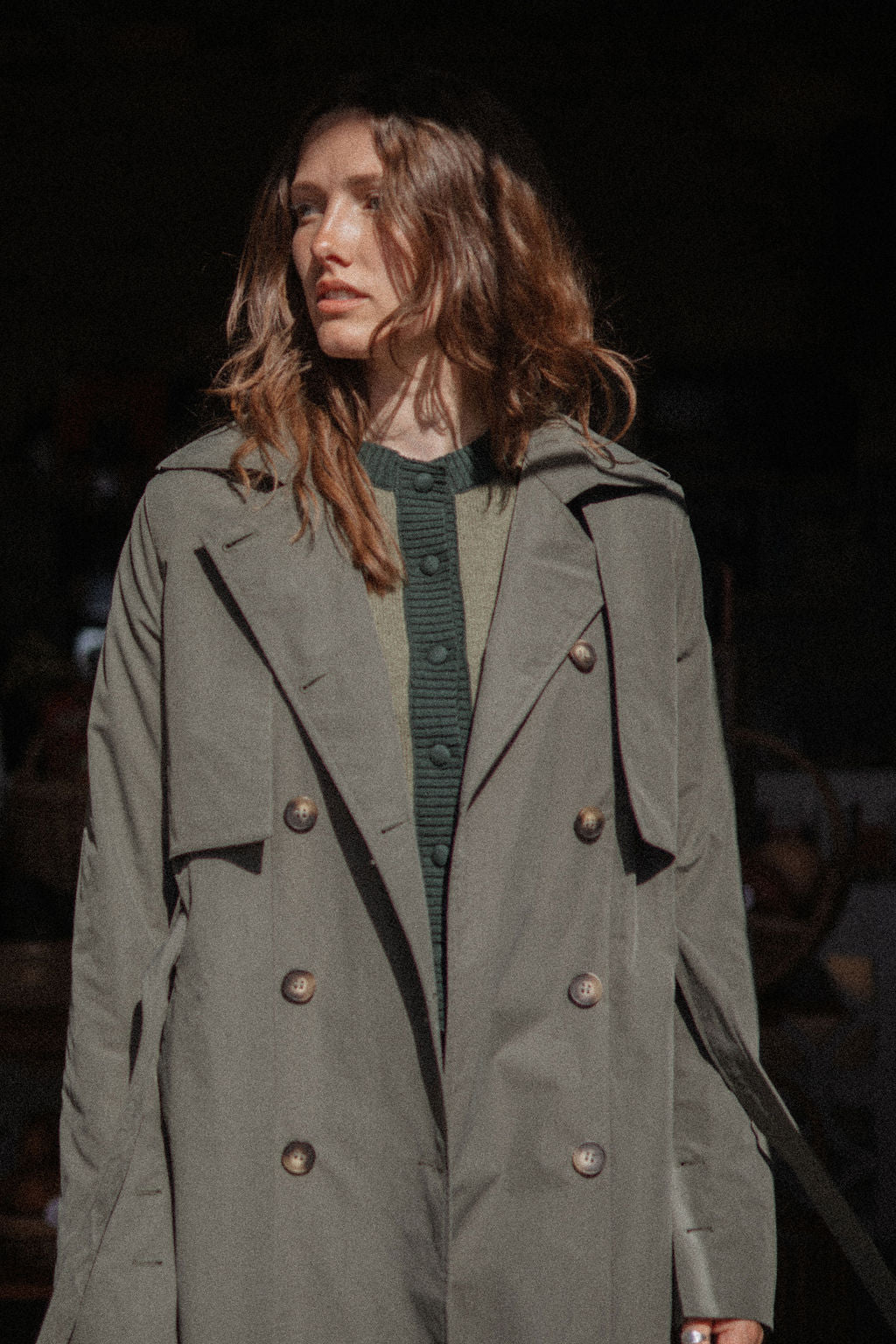 Woman wearing a long green coat with a dark background