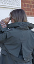 Person wearing a gray jacket with 'Back yourself!' text on the back, standing in front of a building.
