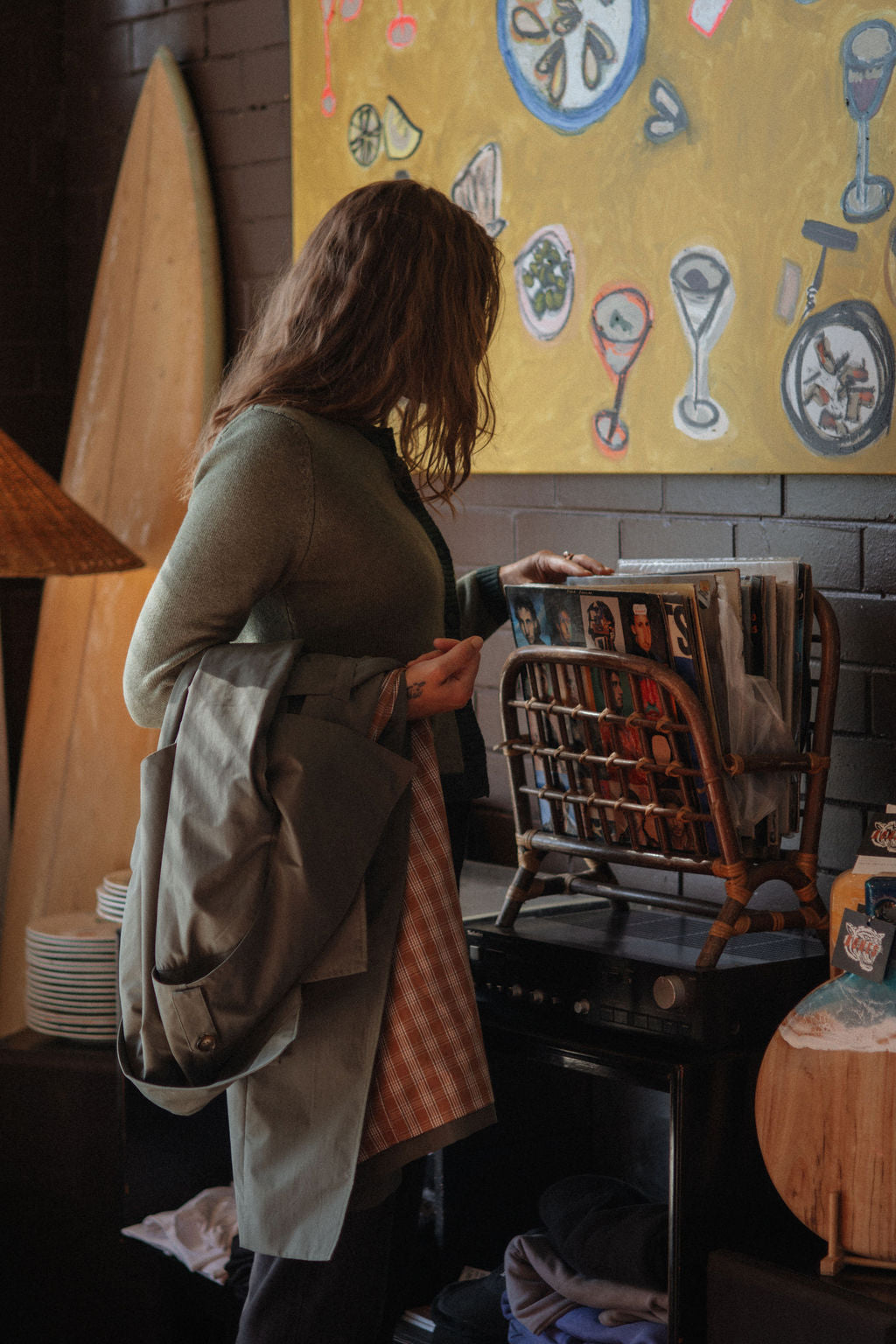 Woman in a green coat standing in a restaurant with a colorful painting on the wall.