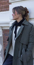 Woman wearing a green coat and black scarf leaning against a building.