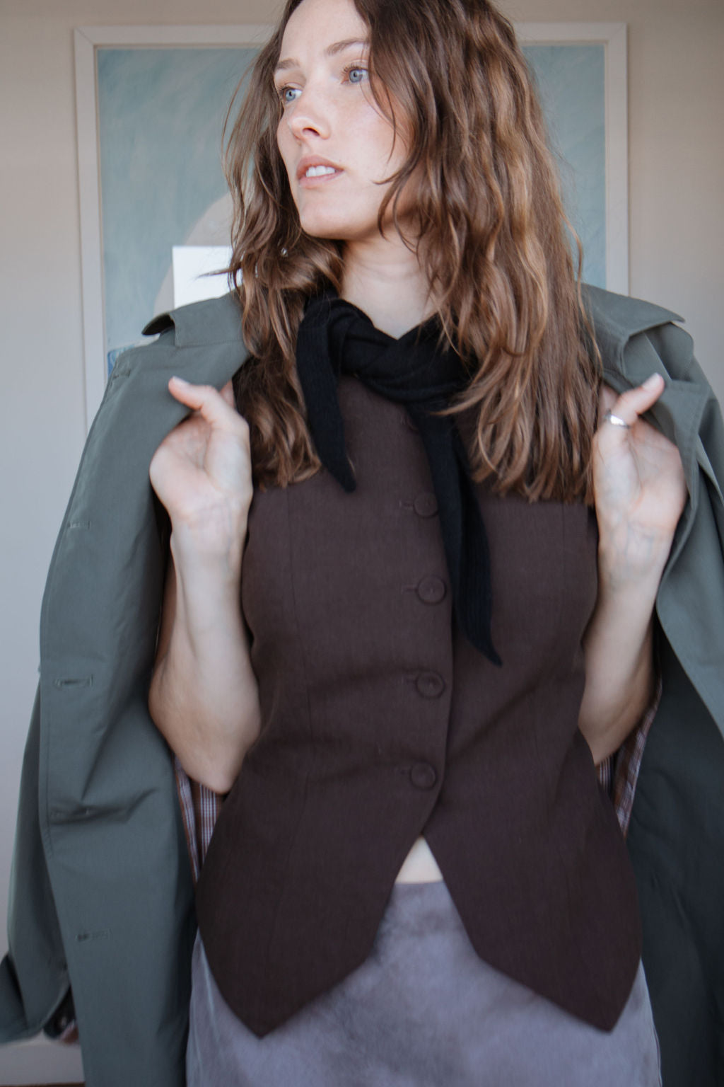 Woman wearing a brown top and olive green coat indoors