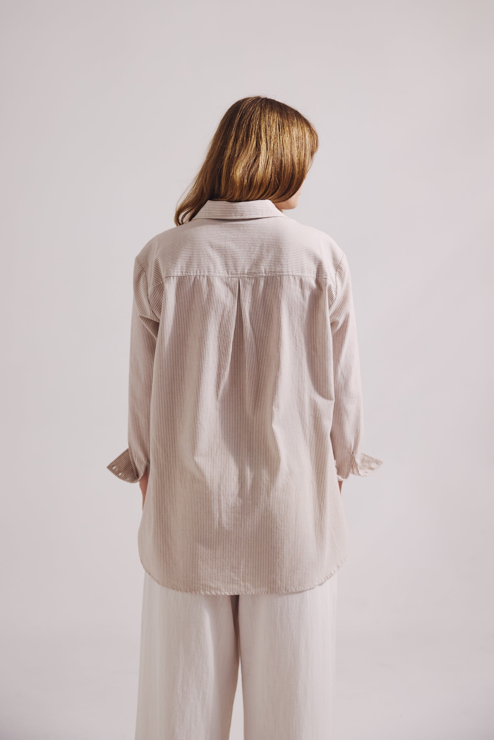 Person wearing a beige shirt and pants against a plain background