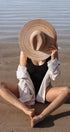 Person sitting on sand wearing a wide-brimmed hat and light shirt.