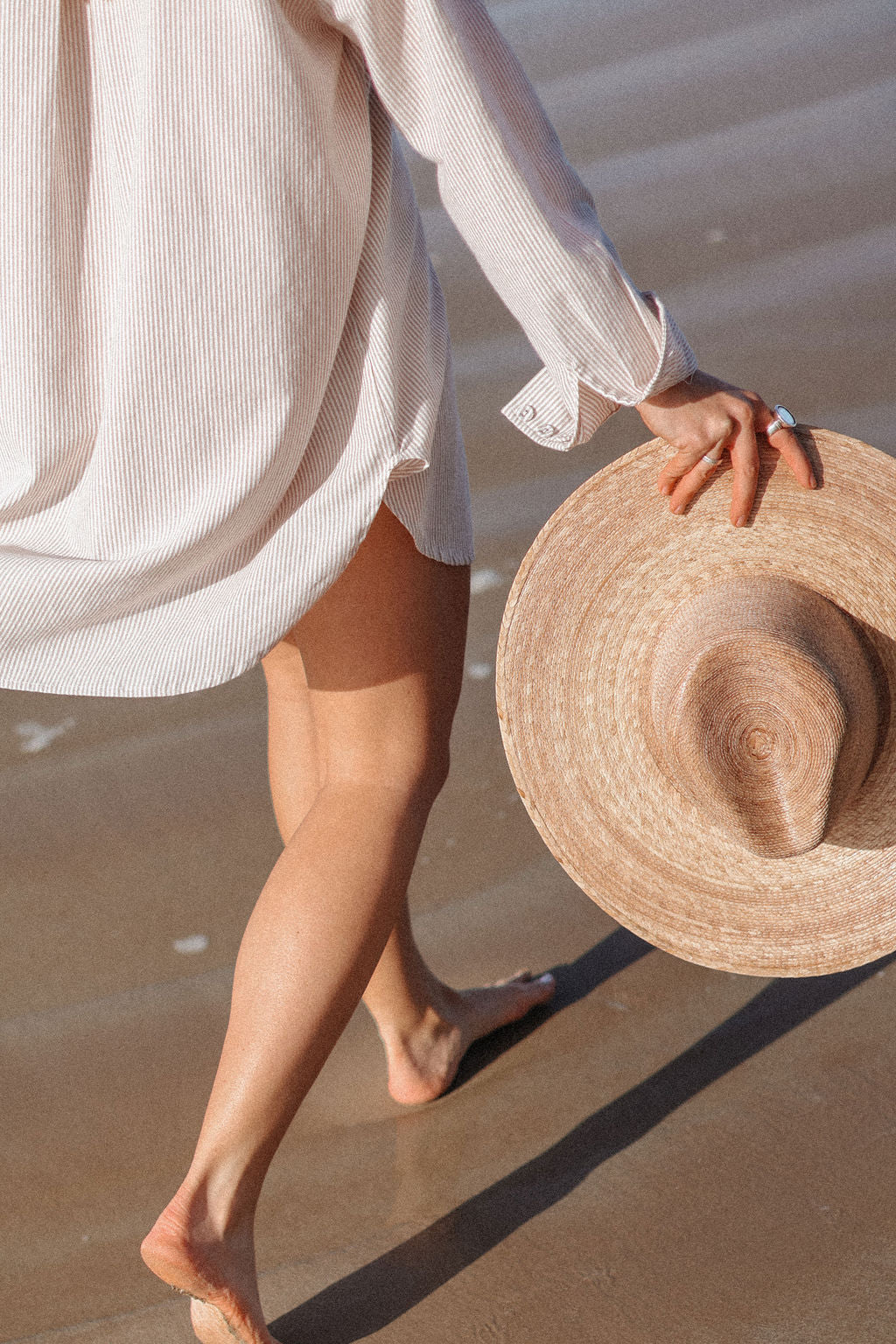 Person holding a straw hat on a beach