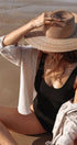 Person wearing a straw hat and black swimsuit sitting on sand