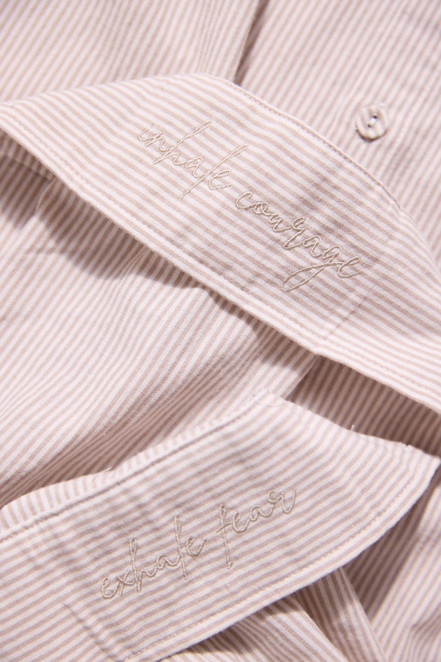 Close-up of a light pink corduroy shirt with embroidered text on the collar and sleeve.