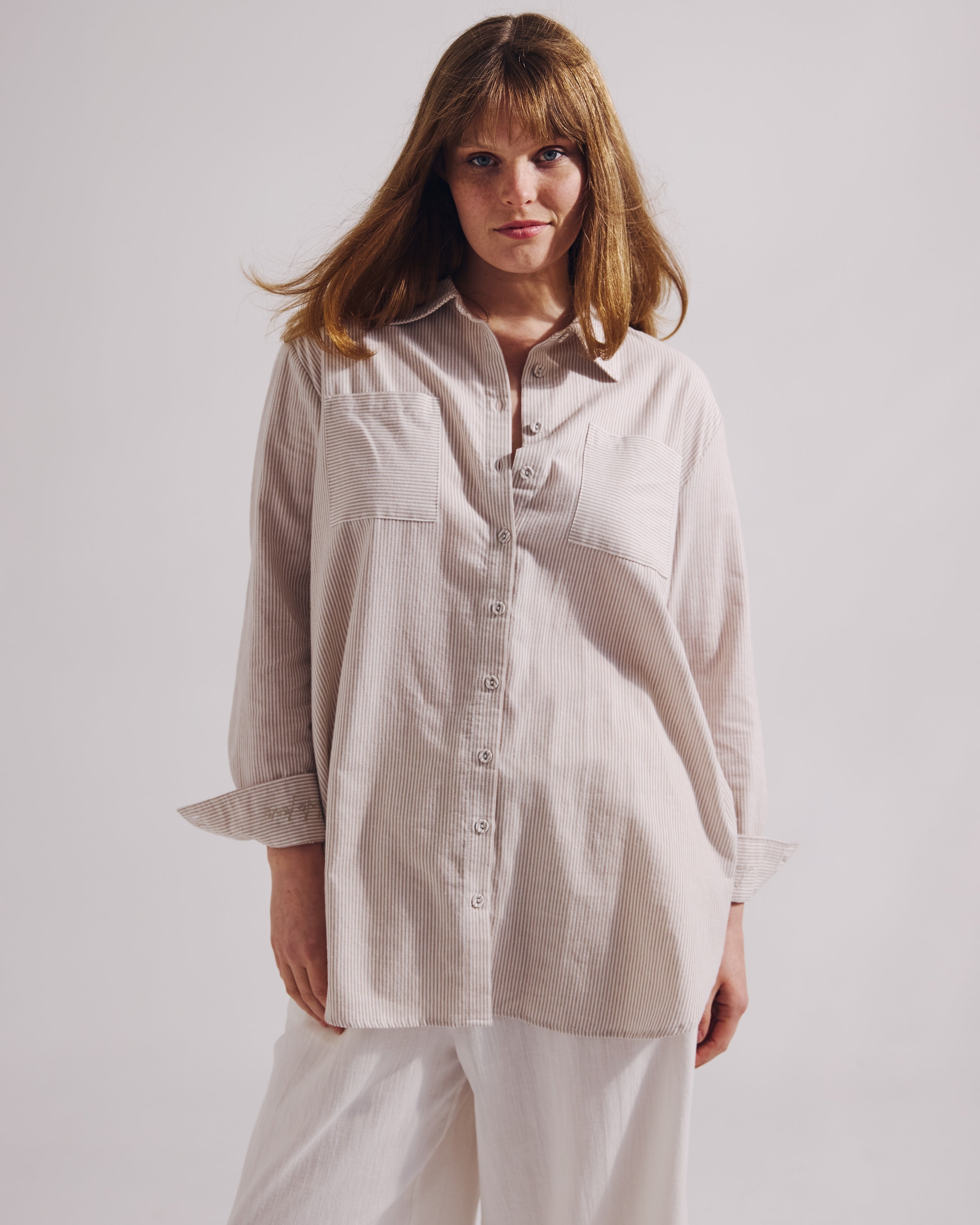 Woman wearing a beige shirt and white pants against a plain background
