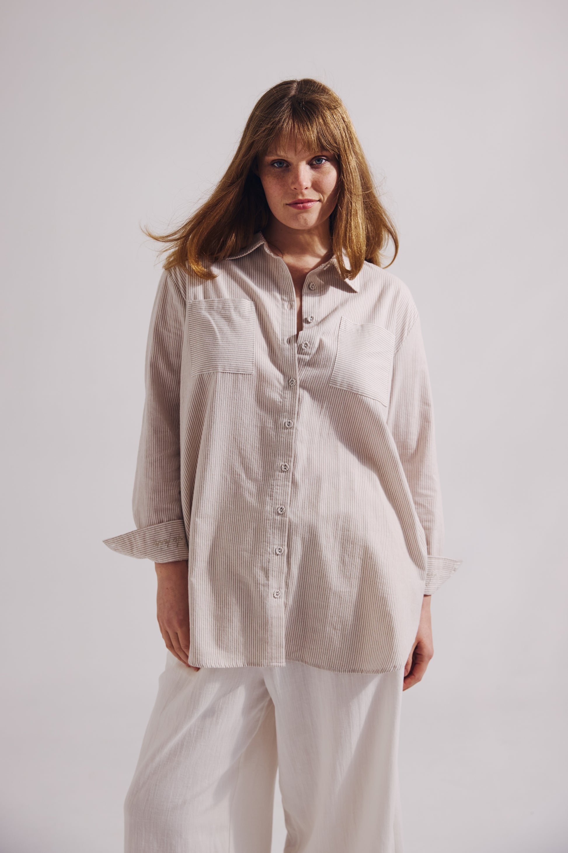 Woman wearing a beige shirt and white pants against a plain background