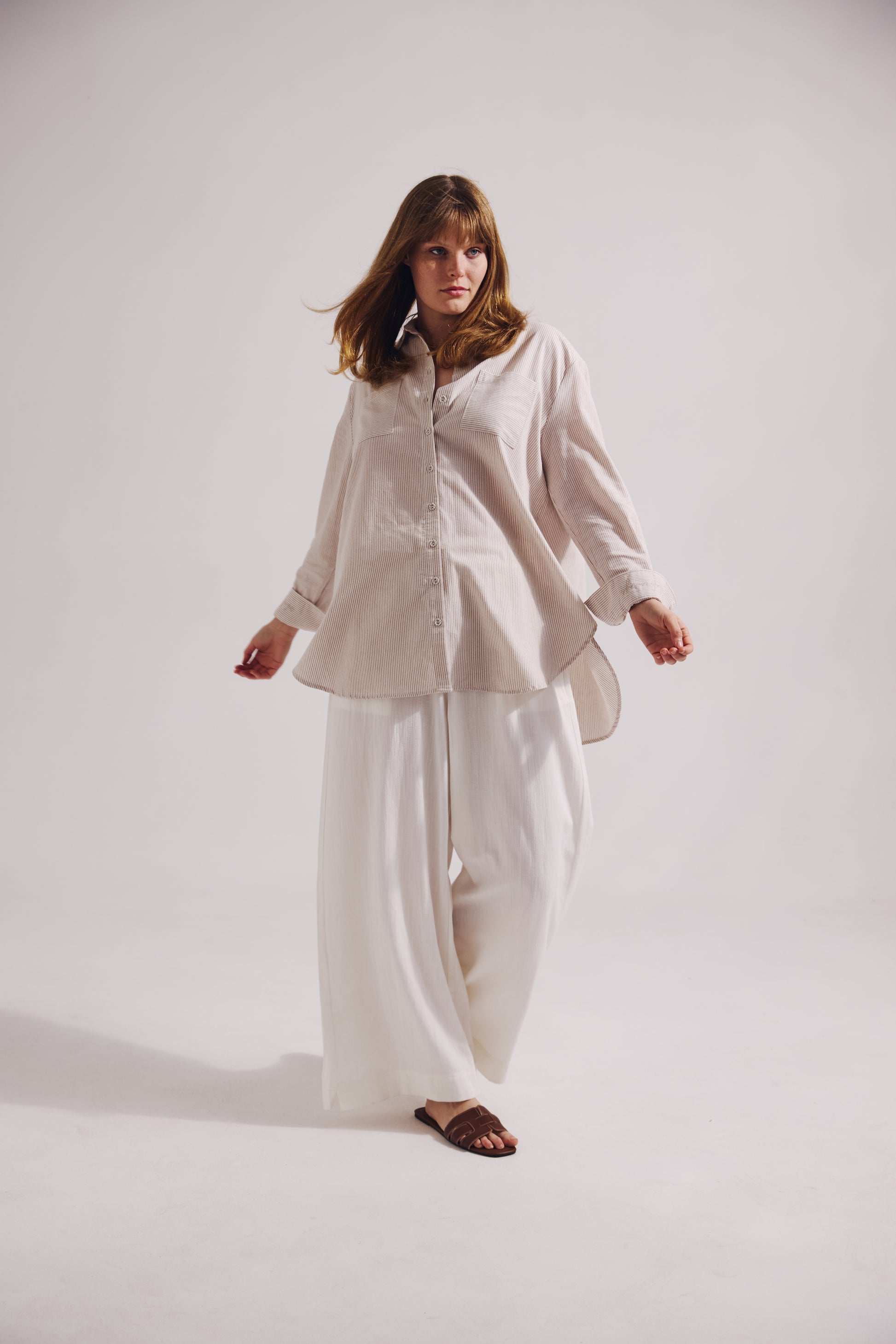 Woman wearing a beige shirt and white pants on a plain background