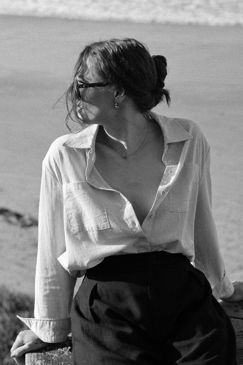 Woman wearing a light-colored shirt and dark pants by a body of water.