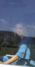 Person sitting inside a vehicle with a scenic reflection on the window