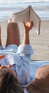 Person reading a book on a beach with a hat nearby