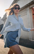 Woman in light blue shirt and shorts walking outdoors with a building in the background