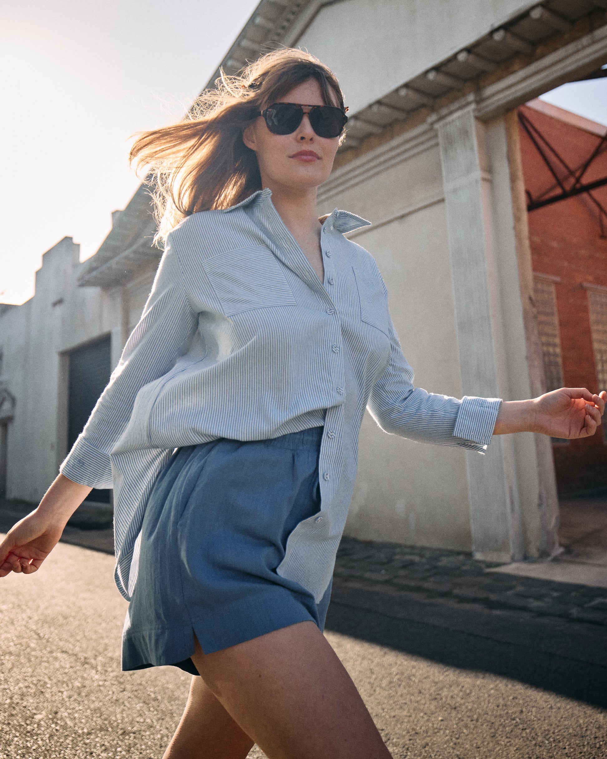 Woman in light blue shirt and shorts walking outdoors with a building in the background