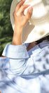 Person wearing a light blue striped shirt and a white sun hat outdoors.