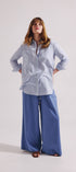 Woman wearing a light blue shirt and wide-leg pants on a white background