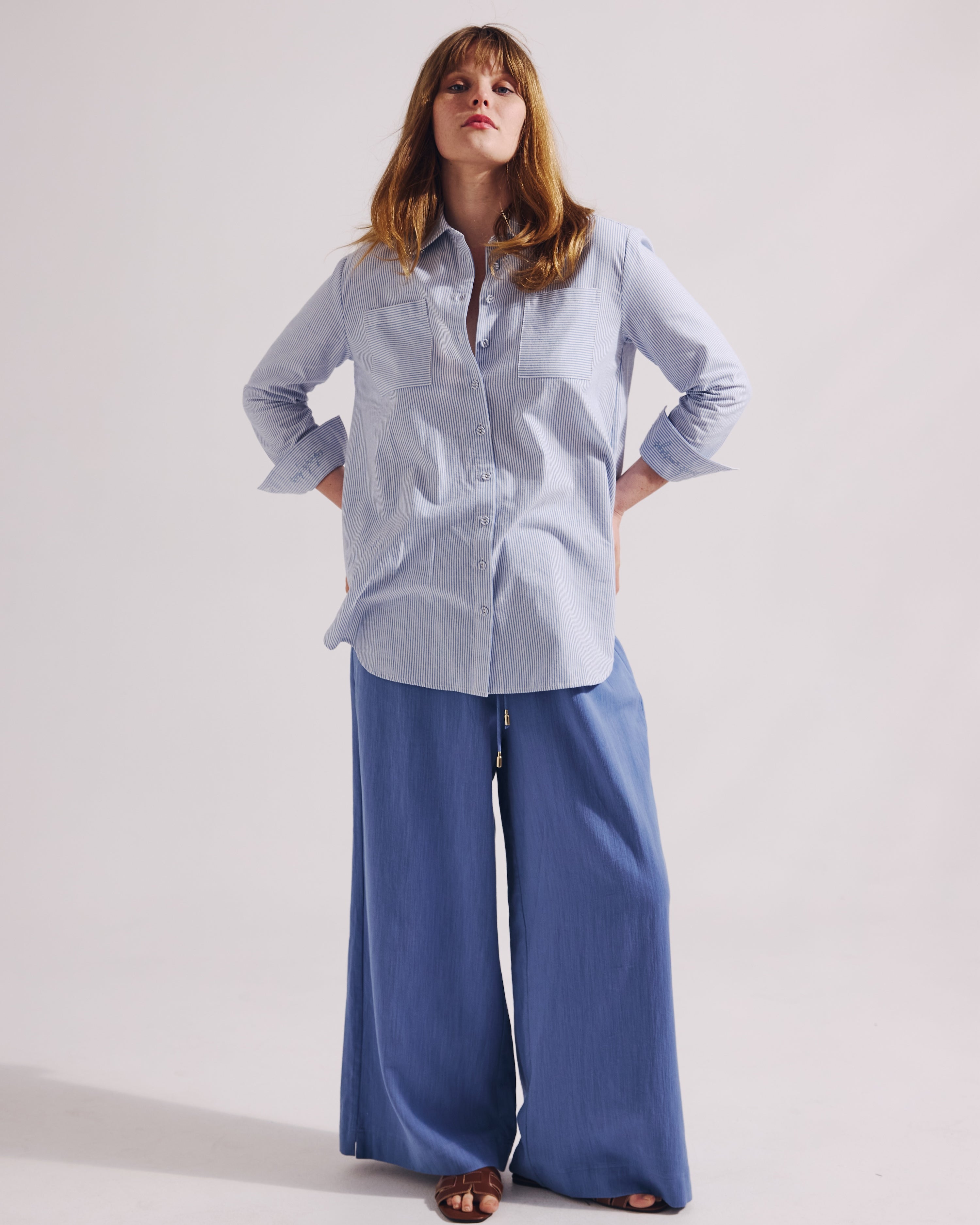 Woman wearing a light blue shirt and wide-leg pants on a white background